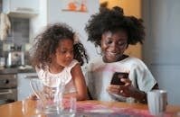 Mother and daughter sharing a joyful moment with a smartphone in the kitchen.